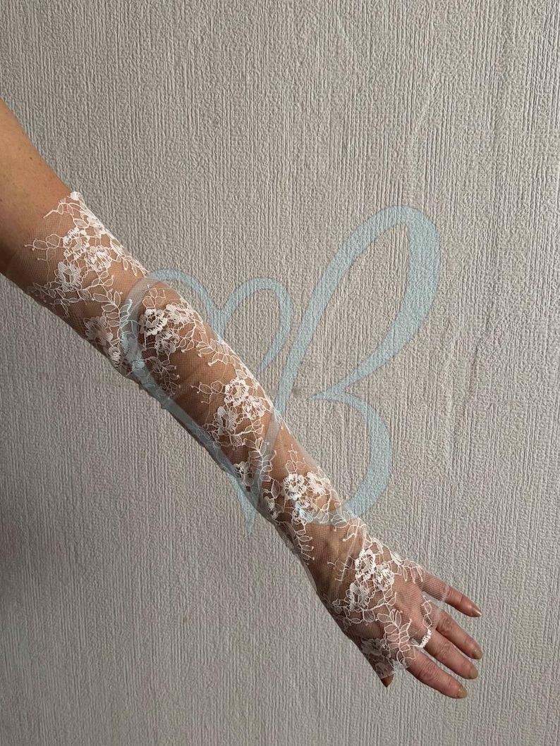K&ouml;nnte beinhalten: Wei&szlig;e Spitzenhandschuhe mit floralen Mustern. Die Handschuhe sind lang und reichen bis zum Arm. Das filigrane Spitzendesign ist sichtbar und erzeugt einen eleganten, romantischen Look. Die Handschuhe sind wahrscheinlich f&uuml;r einen besonderen Anlass.