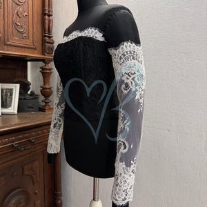 May include: A black off-the-shoulder top with long sleeves made of white lace. The top is fitted and has a delicate lace trim around the neckline.