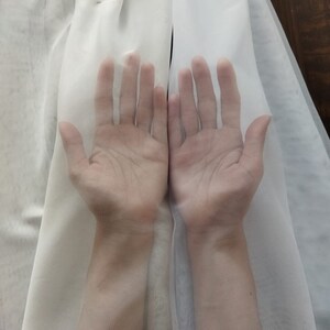 K&ouml;nnte beinhalten: Zwei H&auml;nde sind mit gespreizten Fingern zu sehen, die durch einen durchsichtigen wei&szlig;en Stoff greifen. Der Stoff ist durchscheinend, sodass die H&auml;nde durch ihn hindurch zu sehen sind.