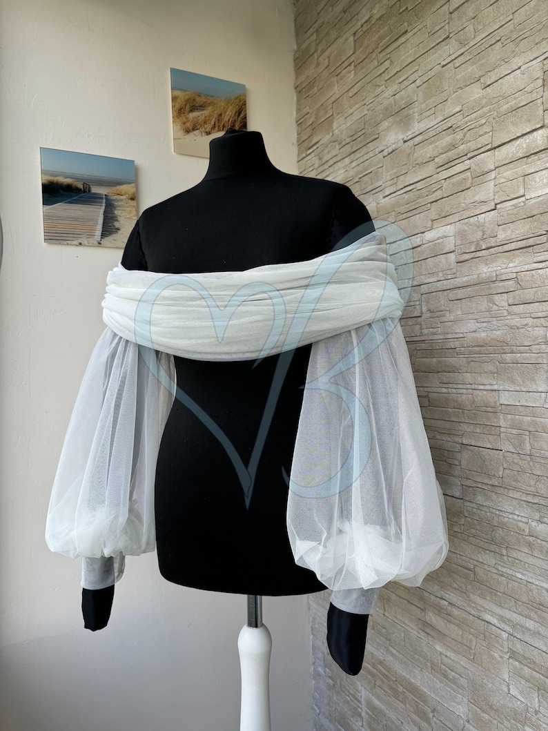 May include: White off-the-shoulder top with sheer, puffy sleeves. The sleeves are made of a delicate, lightweight fabric that adds a touch of elegance to the design.