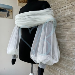 May include: White off-the-shoulder tulle top with long, puffy sleeves. The top is made of a sheer fabric and has a relaxed fit.