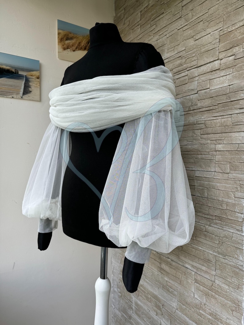 May include: White off-the-shoulder tulle top with long, puffy sleeves. The top is made of a sheer fabric and has a relaxed fit.