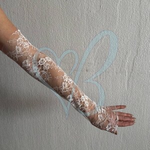 K&ouml;nnte beinhalten: Wei&szlig;e Spitzenhandschuhe mit floralem Muster. Die Handschuhe sind lang und bedecken den Arm bis zum Oberarm. Die Spitze ist filigran und aufwendig, mit einem transparenten Aussehen.