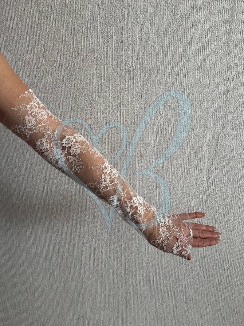 K&ouml;nnte beinhalten: Wei&szlig;e Spitzenhandschuhe mit floralem Muster. Die Handschuhe sind lang und bedecken den Arm bis zum Oberarm. Die Spitze ist filigran und aufwendig, mit einem transparenten Aussehen.