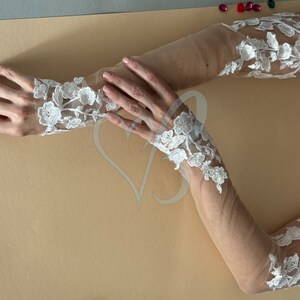 May include: A pair of white lace gloves with sheer fabric. The gloves have a floral design and are long enough to cover the forearms.