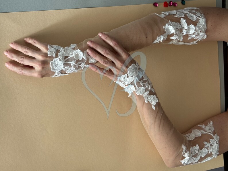 May include: A pair of white lace gloves with sheer fabric. The gloves have a floral design and are long enough to cover the forearms.