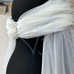 May include: White tulle fabric draped over a black mannequin. The tulle is gathered at the waist and has a beaded embellishment.