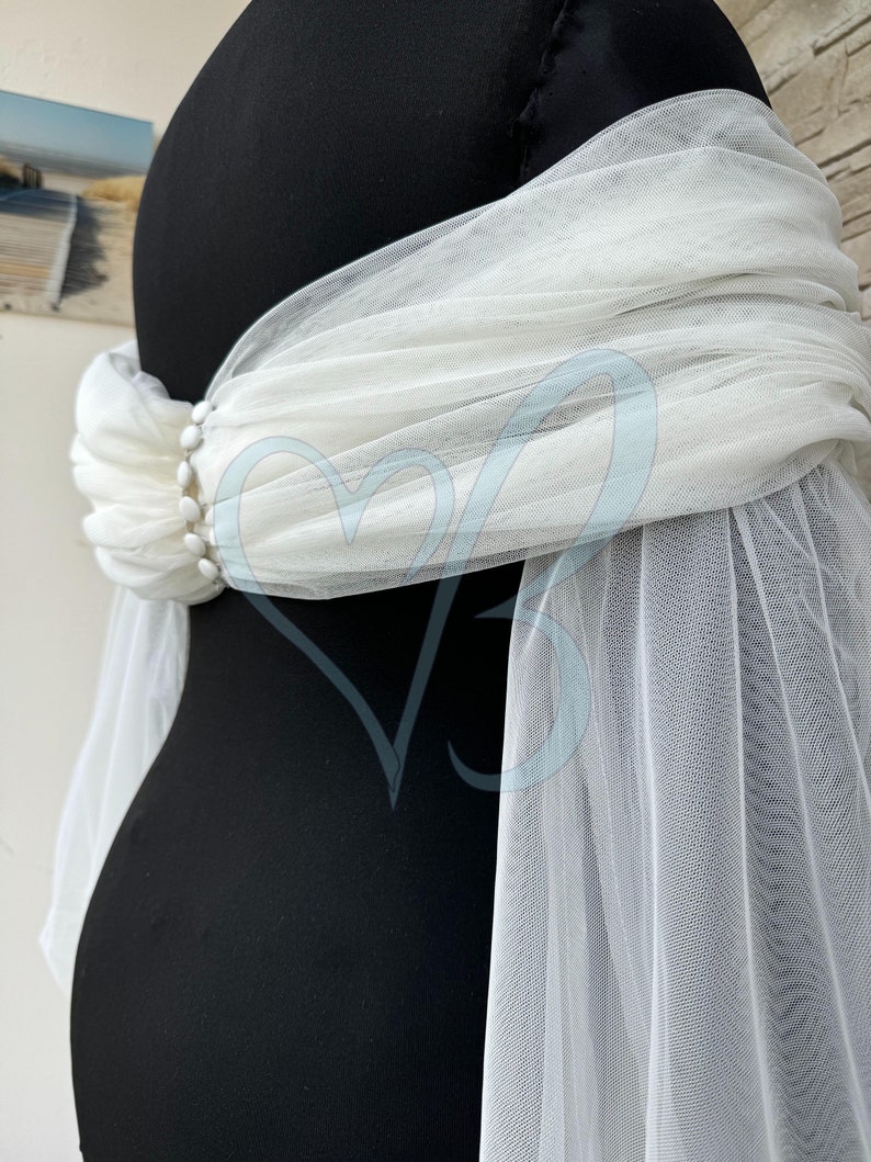 May include: White tulle fabric draped over a black mannequin. The tulle is gathered at the waist and has a beaded embellishment.