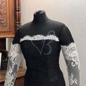 May include: A black dress with a high neckline and long sleeves. The sleeves are made of white lace and the dress has a black lace overlay.