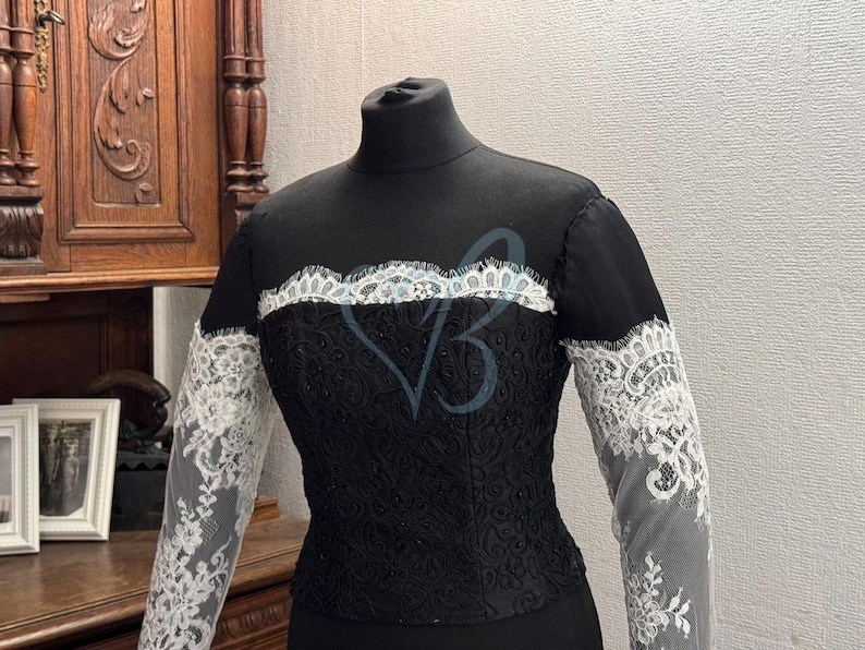 May include: A black dress with a high neckline and long sleeves. The sleeves are made of white lace and the dress has a black lace overlay.