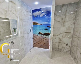 Puede incluir: Un baño con azulejos blancos y una puerta de ducha de vidrio con una imagen impresa de una escena de playa con agua azul, un muelle de madera y un cielo nublado. La puerta de la ducha está enmarcada en plata.