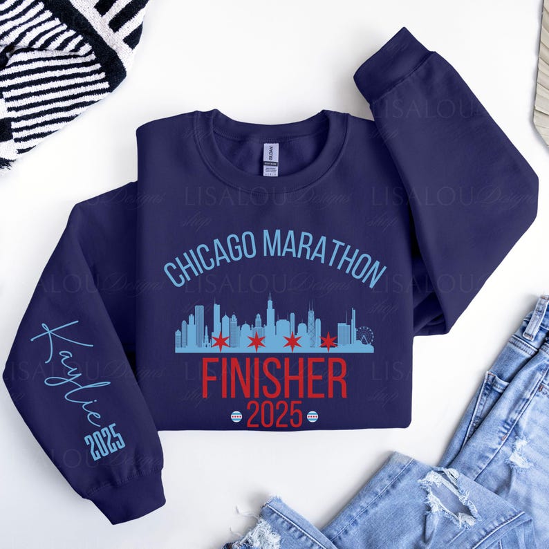 Op de afbeelding: Marineblauw sweatshirt met de tekst "Chicago Marathon Finisher 2025". Het ontwerp bevat een skyline-afbeelding en de naam "Kaylie" met het jaar 2025 op de mouw.