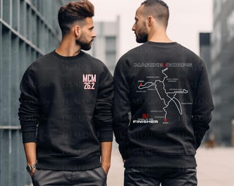 May include: A black crewneck sweatshirt featuring a white and red graphic on the front chest that reads MCM 26.2. The back displays a white map of the Marine Corps Marathon route with the text MARINE CORPS, 26.2, and FINISHER.