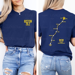May include: Navy blue t-shirt with "BOSTON 26.2" in yellow text on the front. The back features a yellow route map with the text "BOSTON" and "26.2 MILES". The shirt commemorates the Boston Marathon.