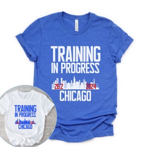 May include: Two t-shirts with a white graphic design that says "Training in Progress" with a skyline of Chicago and the text "26.2 2024 Chicago". The larger shirt is royal blue and the smaller shirt is white.
