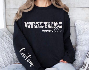 May include: Black sweatshirt with white text that reads "Wrestling mama" with a heart symbol. The text is surrounded by silhouettes of wrestlers. The left sleeve has the word "Custom" written vertically in white.