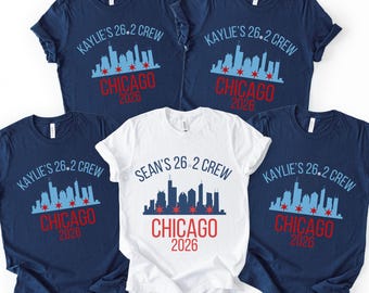 May include: Four navy blue t-shirts and one white t-shirt featuring a Chicago skyline graphic. The navy shirts display the text Kaylie's 26.2 Crew, while the white shirt displays Sean's 26.2 Crew. All shirts include the text Chicago 2026 in red.