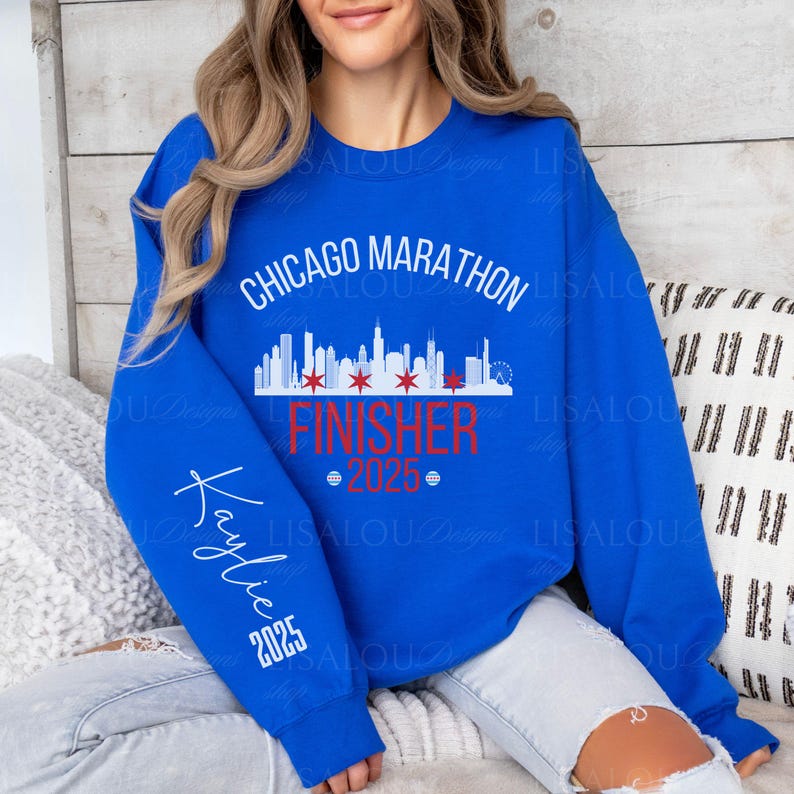Op de afbeelding: Koningsblauw sweatshirt met de tekst "Chicago Marathon Finisher 2025". Het ontwerp bevat een skyline en de naam "Kaylie" op de mouw. Een casual top voor marathonlopers.