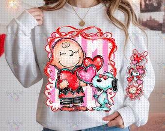Puede incluir: Sudadera blanca con un gráfico colorido de Charlie Brown y Snoopy sosteniendo globos en forma de corazón. El diseño incluye un marco rojo con corazones y un tema de San Valentín.