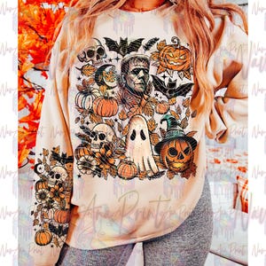 May include: A beige sweatshirt featuring a Halloween-themed graphic. The design includes pumpkins, skulls, bats, a ghost, and Frankenstein's monster. The sleeve has a matching design with skulls, pumpkins, and bats. The text "Anna Printy" is visible.