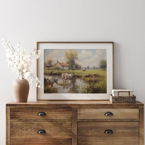 May include: A framed painting of a rural landscape with a white farmhouse, a stream, and cows grazing in a field. The painting is in a wooden frame and is hanging on a white wall.