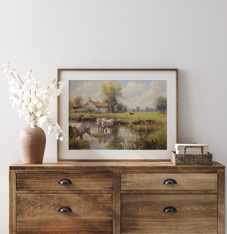 May include: A framed painting of a rural landscape with a white farmhouse, a stream, and cows grazing in a field. The painting is in a wooden frame and is hanging on a white wall.