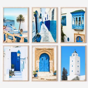 May include: Set of six framed art prints featuring scenes of architecture in shades of blue and white. The images depict buildings, doorways, and alleyways, with a coastal theme. The prints are displayed in wooden frames.