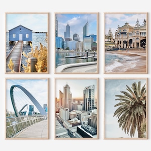 May include: Six framed art prints featuring scenic views. The prints showcase a blue boathouse on a pier, a cityscape with skyscrapers, a beach with a building, a bridge, a city skyline at sunset, and a palm tree.