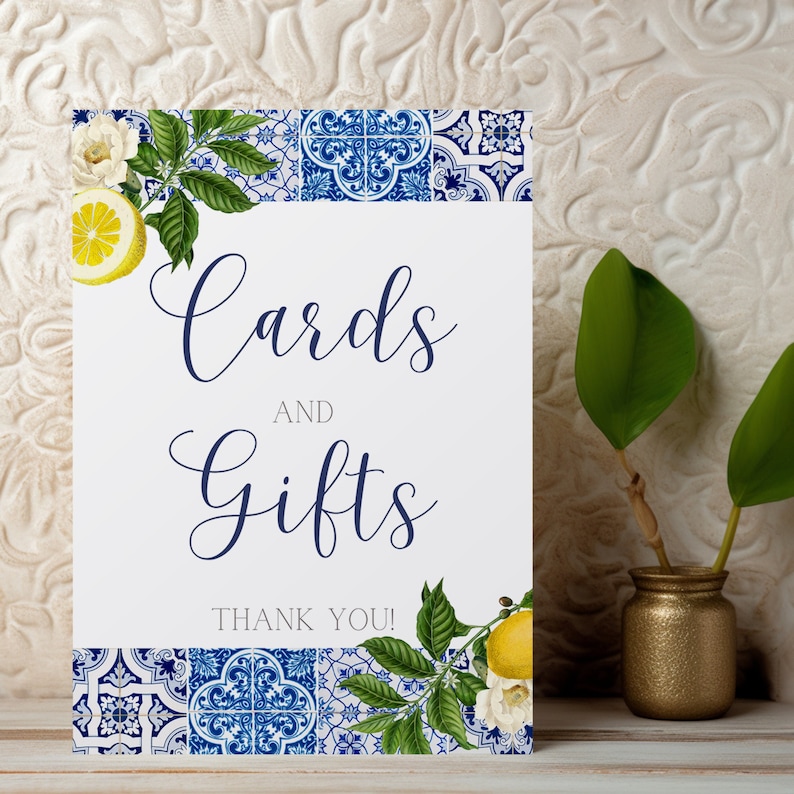May include: A white sign with blue text that reads "Cards and Gifts Thank You!"  The sign is decorated with blue and white tile patterns, lemons, and white flowers.