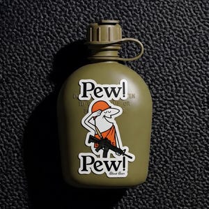 Puede incluir: Una cantimplora de plástico verde oliva con una pegatina que tiene el texto Pew! en la parte superior e inferior. La pegatina muestra un personaje de dibujos animados con sombrero y banda naranja, sosteniendo un rifle negro y el texto Ghost Gear.