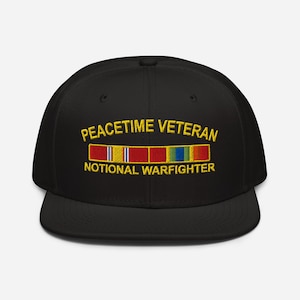 May include: Black baseball cap with embroidered text "PEACETIME VETERAN" and "NOTIONAL WARFIGHTER" in gold. Features a colorful ribbon design. A classic, structured hat.