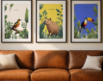 May include: Three framed art prints showcasing illustrations of a bird, a capybara, and a toucan. Each print has a different background colour. The prints are displayed above a brown leather sofa, creating a nature-themed decor.