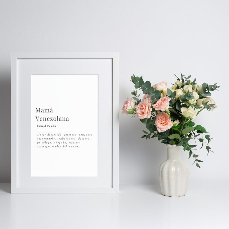 Puede incluir: Una impresi&oacute;n enmarcada con fondo blanco y texto negro. El texto dice "Mam&aacute; Venezolana" y una definici&oacute;n en espa&ntilde;ol. La impresi&oacute;n est&aacute; sobre una superficie blanca con un ramo de rosas rosas y blancas en un jarr&oacute;n blanco.