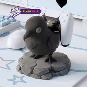 May include: A black bird-shaped controller stand holding a white controller. The stand is gray and sits on a gray rock-like base. The words "NEW ARRIVAL" and "FLASH SALE" are visible in the top left.