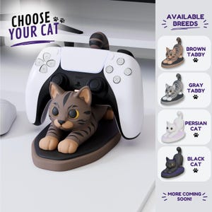 Puede incluir: Un soporte para mando con forma de gato atigrado marrón que sostiene un mando de juego blanco y negro. El texto CHOOSE YOUR CAT aparece en la parte superior, con una barra lateral que muestra las razas disponibles: Brown Tabby, Gray Tabby, Persian Cat y Black Cat.