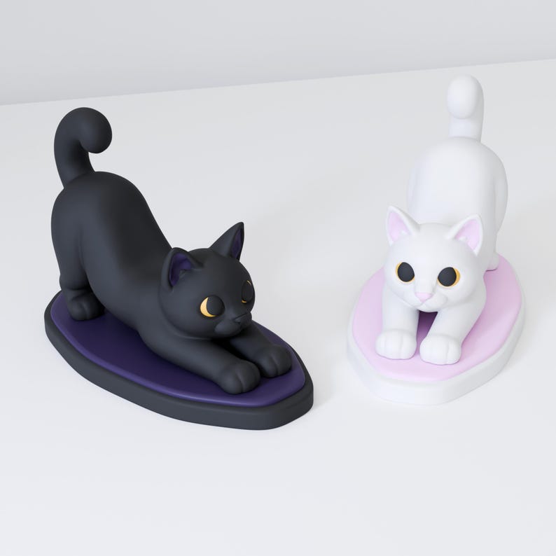 May include: Two cat figurines in a stretching pose. One is a solid black cat on a dark purple oval base with yellow eyes. The other is a solid white cat on a light pink oval base with yellow eyes. Both cats have arched backs and tails raised.