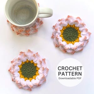 May include: A white mug rests on a white and peach crochet coaster, with two more flower-shaped coasters. The coasters feature a green centre, yellow ring, and white and peach petals. The text "CROCHET PATTERN Downloadable PDF" is in a white circle.