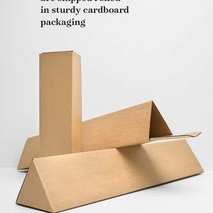 Puede incluir: Primer plano de tres cajas de cart&oacute;n marr&oacute;n, una de pie y dos tumbadas. Las cajas se utilizan para enviar impresiones de p&oacute;ster enrolladas. El texto "All poster prints (unframed) are shipped rolled in sturdy cardboard packaging" es visible en la parte superior de la imagen.