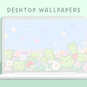 May include: A laptop screen displaying a digital desktop wallpaper with a light blue background and a field of green frogs and pastel flowers. The text "DESKTOP WALLPAPERS" is at the top of the screen.