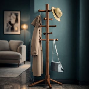 May include: A wooden coat rack with multiple pegs, holding a beige coat, a straw hat, and a light blue purse. The rack has a tripod base and is set against a teal wall. The room has a sofa and a framed picture.