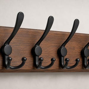 May include: A wooden coat rack with four black metal hooks. The rack is made of dark brown wood and has a rectangular shape. The hooks are curved and have a rounded end.