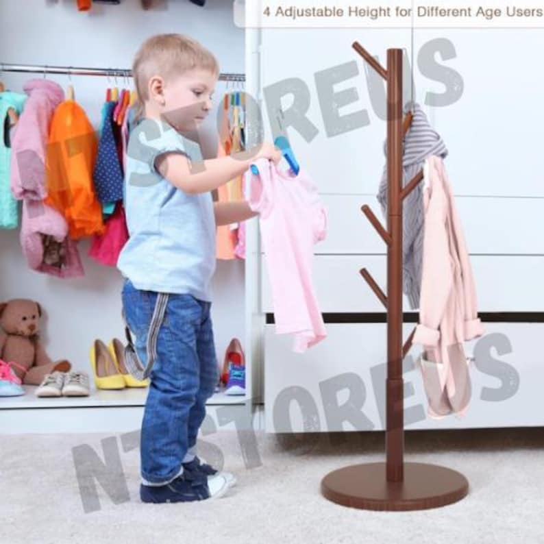 May include: A brown wooden coat rack with four adjustable heights. The rack has six branches for hanging clothes. A young child is standing next to the rack, holding a pink shirt.