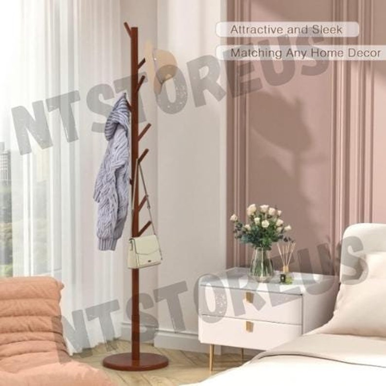 May include: A brown wooden coat rack with multiple branches for hanging clothes and accessories. The rack is standing in a room with a white wall and a white nightstand with two drawers. The text "Attractive and Sleek" and "Matching Any Home Decor" is visible in the image.
