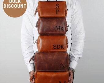 May include: A stack of five brown leather toiletry bags, each with a zipper closure and personalized initials. The bags vary in shade from light to dark brown. The words "BULK DISCOUNT" are in a brown circle in the upper left corner.