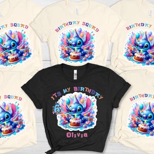May include: Several t-shirts with a vibrant design of a blue alien holding a birthday cake. The shirts are in black and cream, with the words "Birthday Squad" and "It's My Birthday" printed on them. A fun, colourful design.
