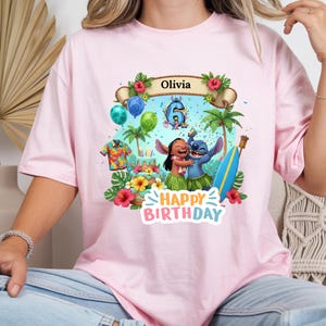 May include: Pink t-shirt featuring a colorful graphic of Lilo and Stitch celebrating a birthday. The design includes a banner with the name "Olivia", balloons, a cake, and the words "Happy Birthday".