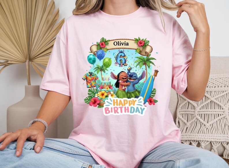 May include: Pink t-shirt featuring a colorful graphic of Lilo and Stitch celebrating a birthday. The design includes a banner with the name "Olivia", balloons, a cake, and the words "Happy Birthday".