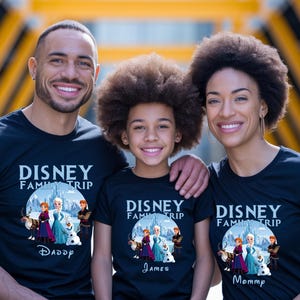 May include: Three people wearing matching black t-shirts with the text "DISNEY FAMILY TRIP" and a graphic from the movie Frozen. The shirts are labeled "Daddy", "James", and "Mommy". The family is smiling.