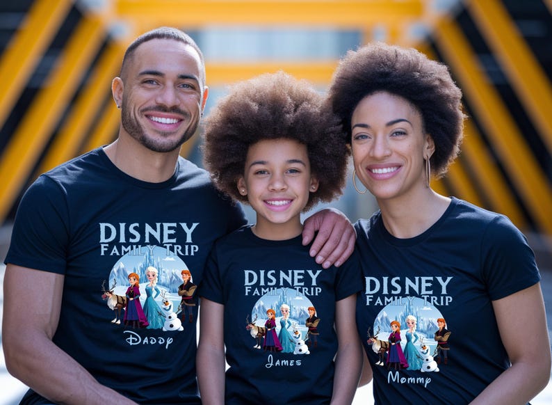 May include: Three people wearing matching black t-shirts with the text "DISNEY FAMILY TRIP" and a graphic from the movie Frozen. The shirts are labeled "Daddy", "James", and "Mommy". The family is smiling.