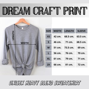 May include: A light gray unisex heavy blend sweatshirt displayed on a wooden hanger. The image includes a size chart with measurements in centimeters for width, length, and sleeve length. The text "DREAM CRAFT PRINT" and "UNISEX HEAVY BLEND SWEATSHIRT" are visible.